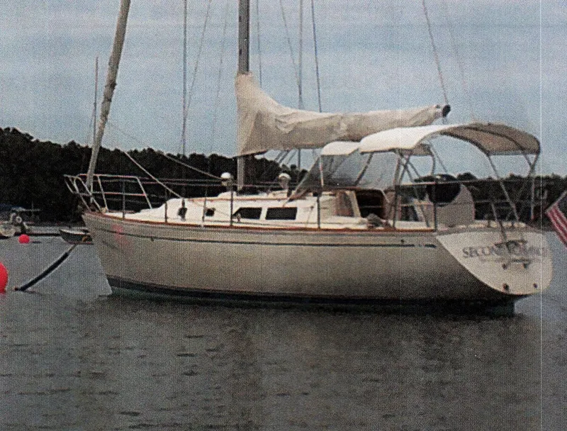 Slide: The Image of 1988 CAL Sloop sailboat anchored on calm water with forested shoreline. - 30