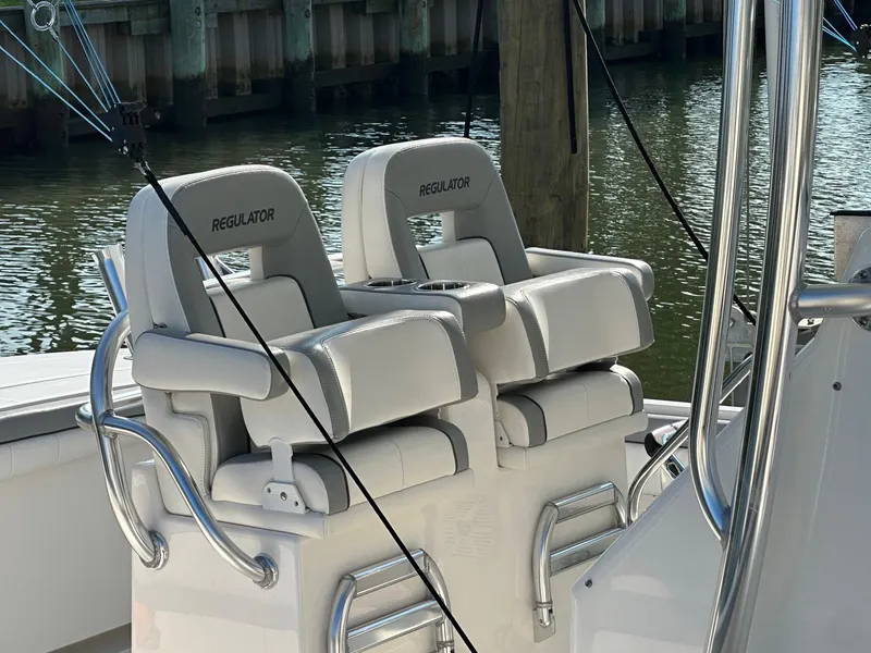 Slide: The Image of 2019 Regulator 28 boat seats with armrests and cup holders, docked by the water. - 9