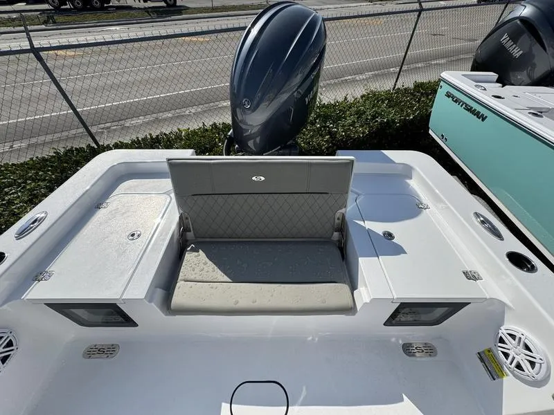Slide: The Image of 2025 Sportsman Masters 227 boat with cushioned seating and outboard motor, parked near a fence. - 21