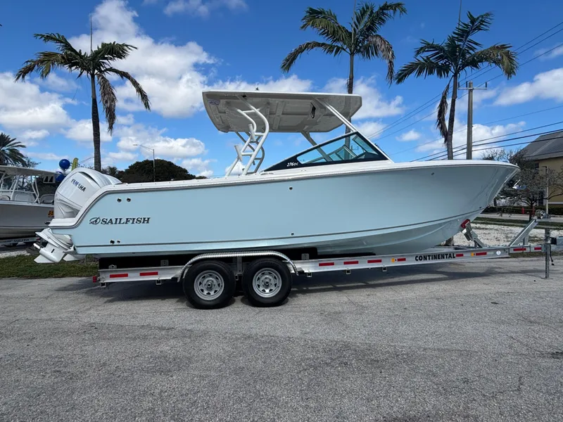 Slide: The Image of 2025 Sailfish 276 DC boat on trailer, parked with palm trees in background. - 0