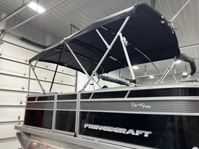 Slide: The Image of 2023 Princecraft Brio Electric 170 pontoon boat with canopy in a garage setting. - 1