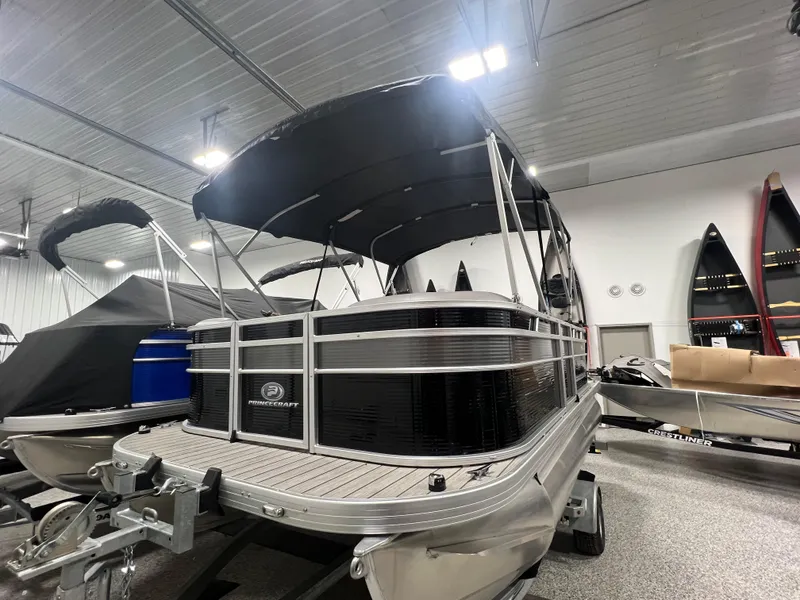 Slide: The Image of 2023 Princecraft Brio Electric 170 pontoon boat in showroom, featuring sleek design and canopy. - 2