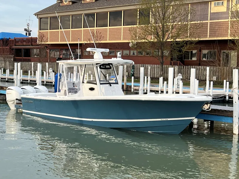 Slide: The Image of 2023 Regulator 34 boat docked in marina, blue hull, white cabin, calm water. - 2