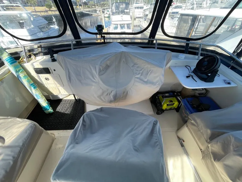 Slide: The Image of 2005 Mainship 430 Aft Cabin Trawler helm with covered seats and marina view. - 24