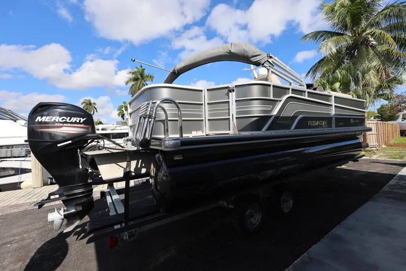 Slide: The Image of 2017 Ranger Reata 200F pontoon boat with Mercury outboard, parked on trailer, palm trees in background. - 22