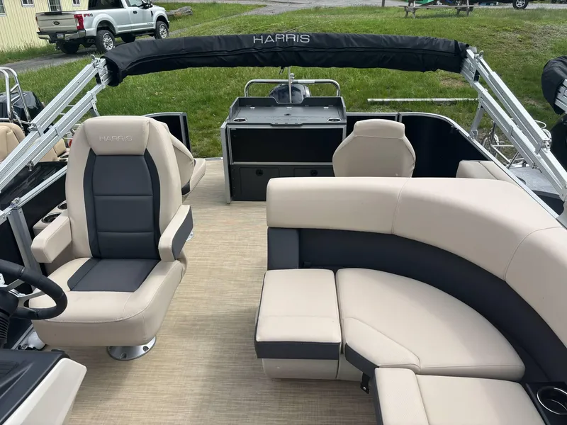 Slide: The Image of 2025 Harris Cruiser 230 pontoon boat interior with beige and gray seating, steering console, and open deck. - 2