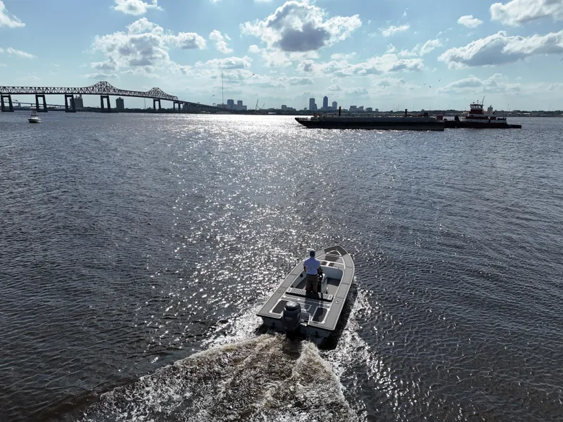 Slide: The Image of 1996 Hewes 18 Redfisher boat cruising on a sunny river near a bridge and barge. - 4
