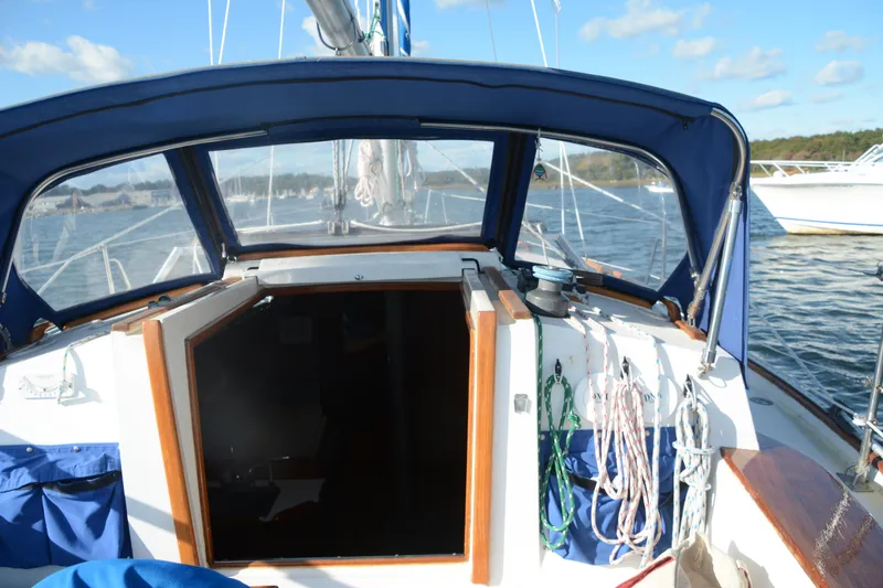 Slide: The Image of 1982 Morgan 32 sailboat cockpit with blue canopy, ropes, and open cabin door on calm water. - 4