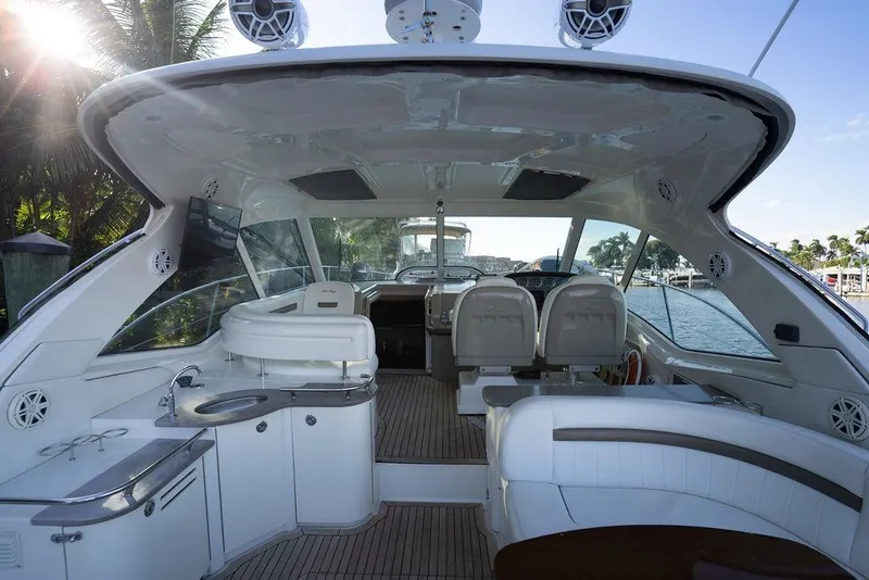 Slide: The Image of 2005 Sea Ray 48 Sundancer yacht interior with seating, kitchenette, and helm, docked by palm trees. - 55