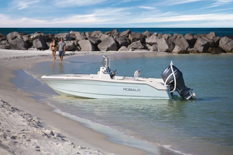 Slide: The Image of 2025 Robalo R160 Center Console boat on a sandy beach with rocky background. - 9