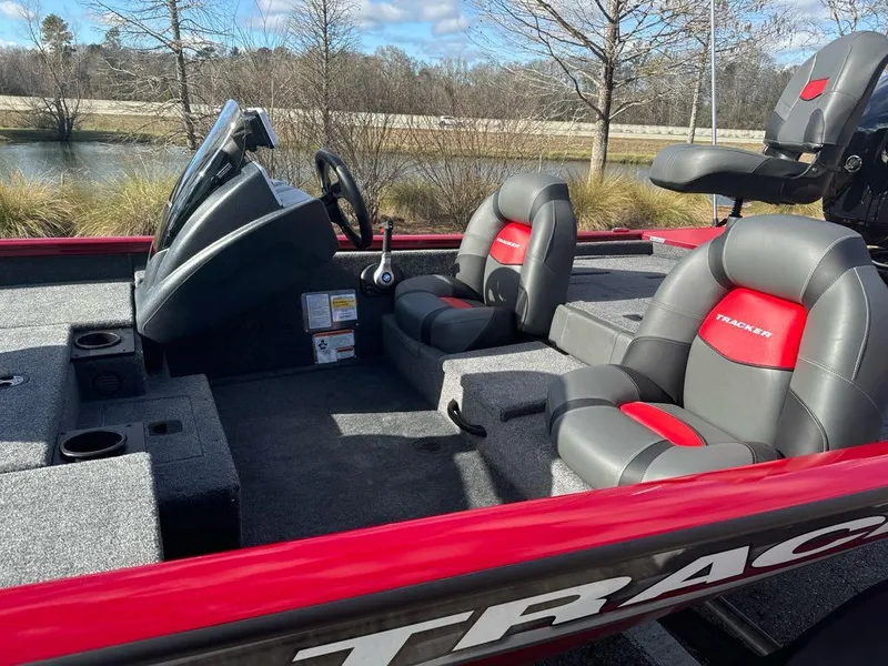 Slide: The Image of 2025 Tracker Pro Team 175 boat interior with gray and red seating, near a lake. - 5