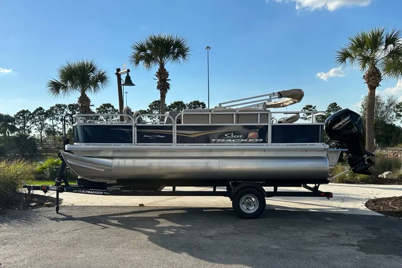 The Image of 2025 Sun Tracker Bass Buggy 18 DLX pontoon boat on trailer, parked outdoors. - 0