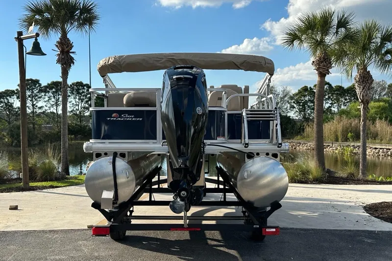 Slide: The Image of 2025 Sun Tracker Bass Buggy 18 DLX pontoon boat on trailer, parked near palm trees. - 3