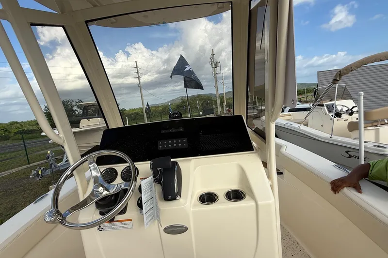 Slide: The Image of 2026 Scout 215 XSF boat helm with steering wheel and control panel, docked outdoors. - 7