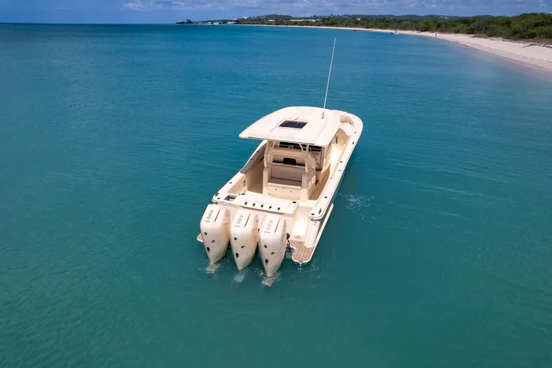 Slide: The Image of 2024 Scout 377 LXF boat cruising in clear turquoise waters near a sandy beach. - 11