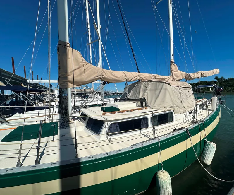 Slide: The Image of 1981 Islander Freeport Ketch sailboat docked, featuring beige sails and green accents under clear blue sky. - 4