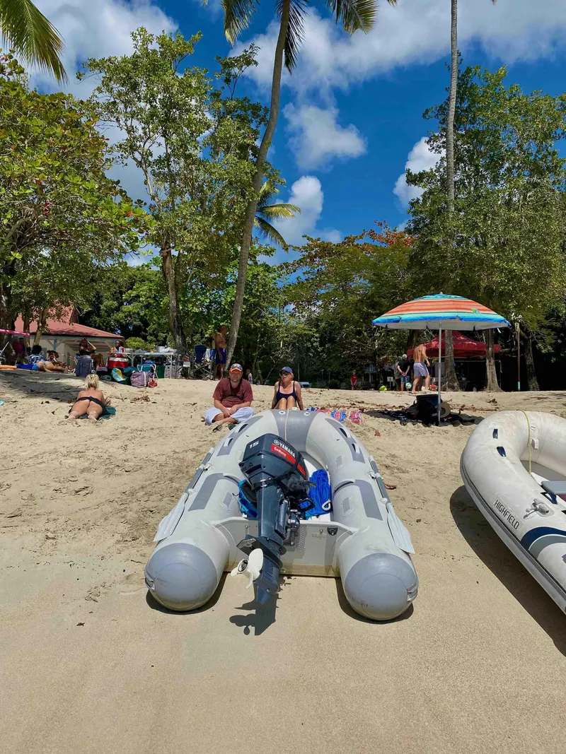 Slide: The Image of Inflatable boat on sandy beach with people relaxing under umbrellas, surrounded by lush trees. - 8