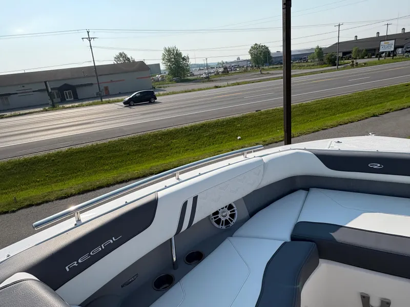 Slide: The Image of 2025 Regal LS9 Surf boat interior with sleek seating, parked near a highway. - 15