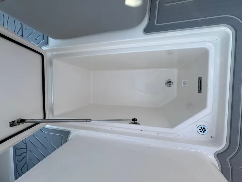 Slide: The Image of 2025 Regal LS9 Surf boat storage compartment, open lid, white interior, drain visible. - 18