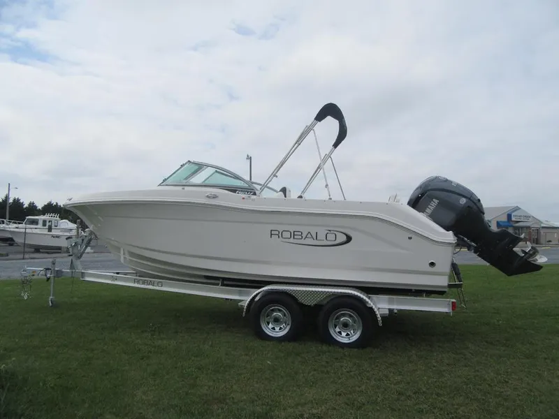 Slide: The Image of 2025 Robalo R207 Dual Console boat on trailer, parked on grass. - 2