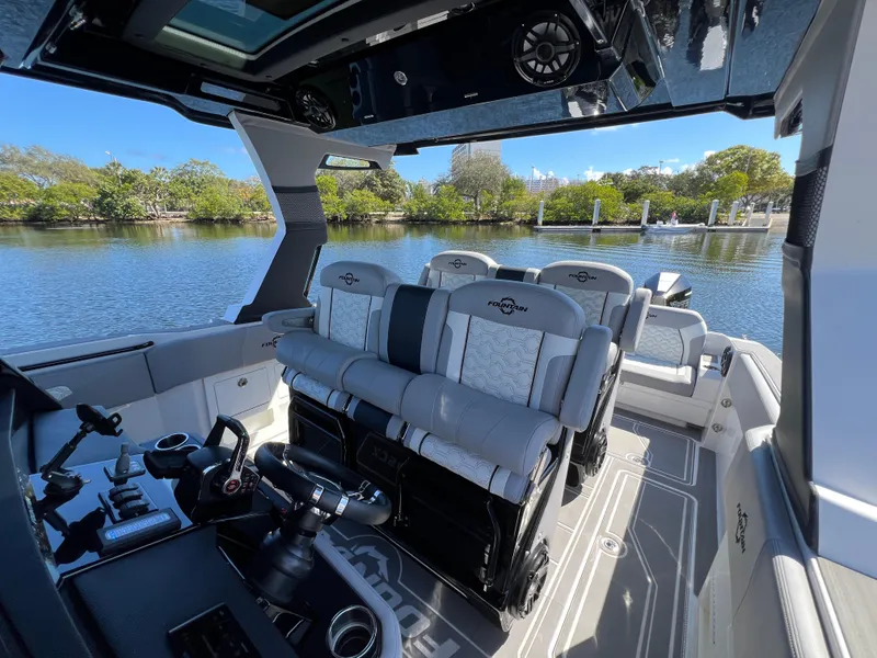 Slide: The Image of 2023 Fountain 38 SCX boat interior with modern seating and controls on a calm waterway. - 17