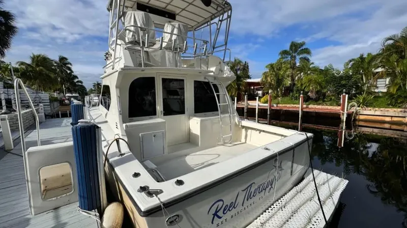 Slide: The Image of 1987 Blackfin Convertible boat docked, featuring spacious deck and upper seating, surrounded by lush greenery. - 4