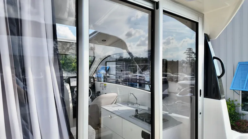Slide: The Image of 2025 Bayliner TROPHY 25 EXPLORER interior view through glass doors, showcasing helm and kitchenette. - 8