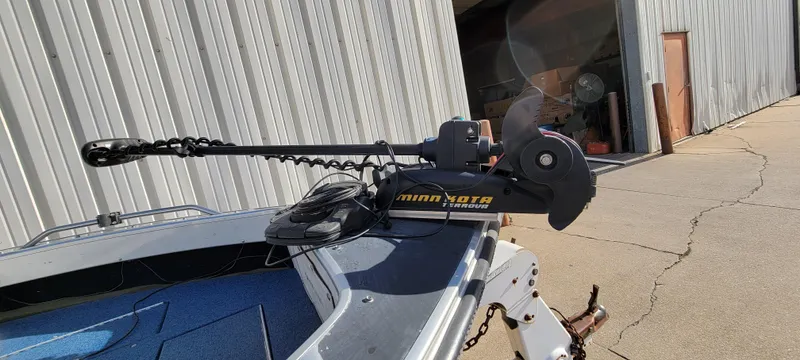 Slide: The Image of 1995 Crestliner Sportfish 1750 with Minn Kota trolling motor, parked near a metal building. - 10