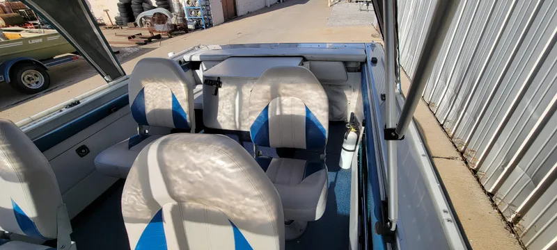 Slide: The Image of 1995 Crestliner Sportfish 1750 interior with blue and white seating, docked near a metal building. - 15