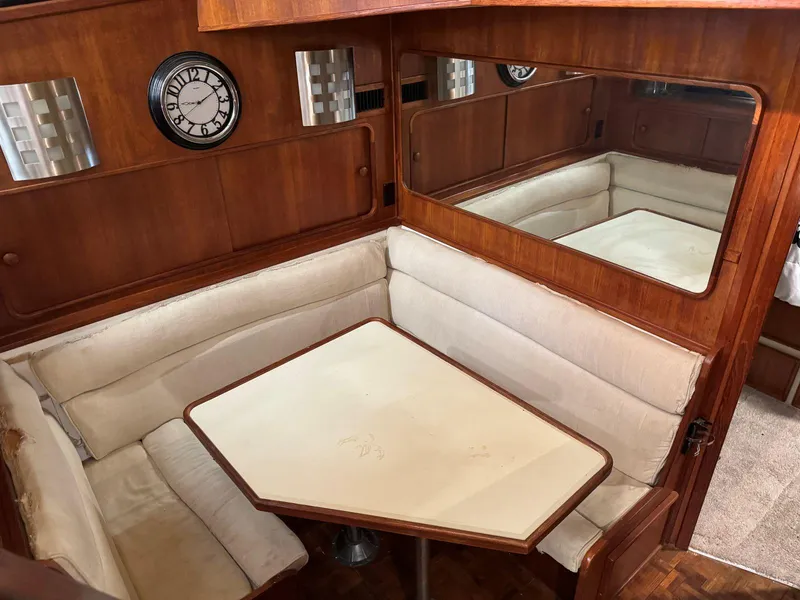 Slide: The Image of 1988 Chris-Craft 426 Catalina interior with cushioned seating, wooden table, and wall clock. - 25