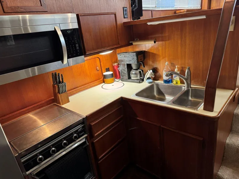 Slide: The Image of 1988 Chris-Craft 426 Catalina kitchen with microwave, stove, sink, and wooden cabinetry. - 27