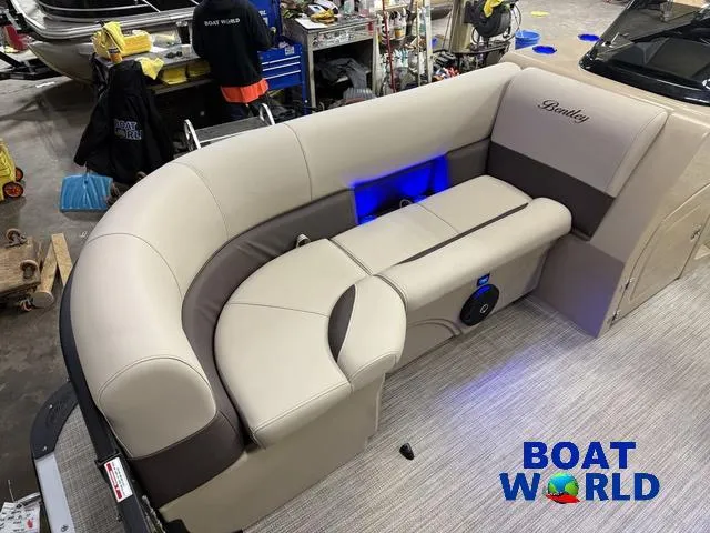 Slide: The Image of 2025 Bentley Pontoons Legacy 223 Navigator interior with beige seating, blue lighting, and Boat World logo. - 8