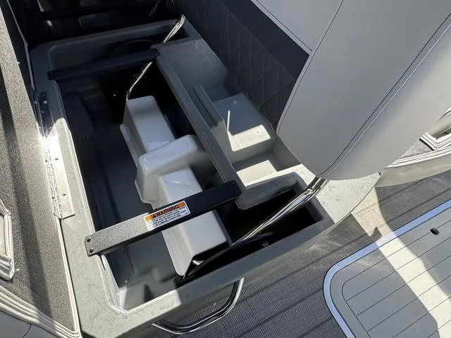 Slide: The Image of 2025 Starcraft CX 23 RL boat storage compartment with seat and safety warning label. - 35