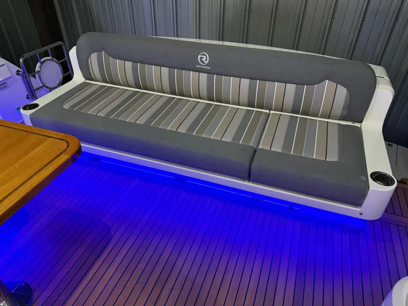 Slide: The Image of 2019 Riviera 4800 Sport Yacht interior with cushioned seating and ambient blue lighting. - 18