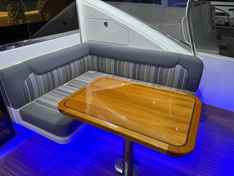Slide: The Image of 2019 Riviera 4800 Sport Yacht interior with elegant seating and wooden table, illuminated by blue lighting. - 19