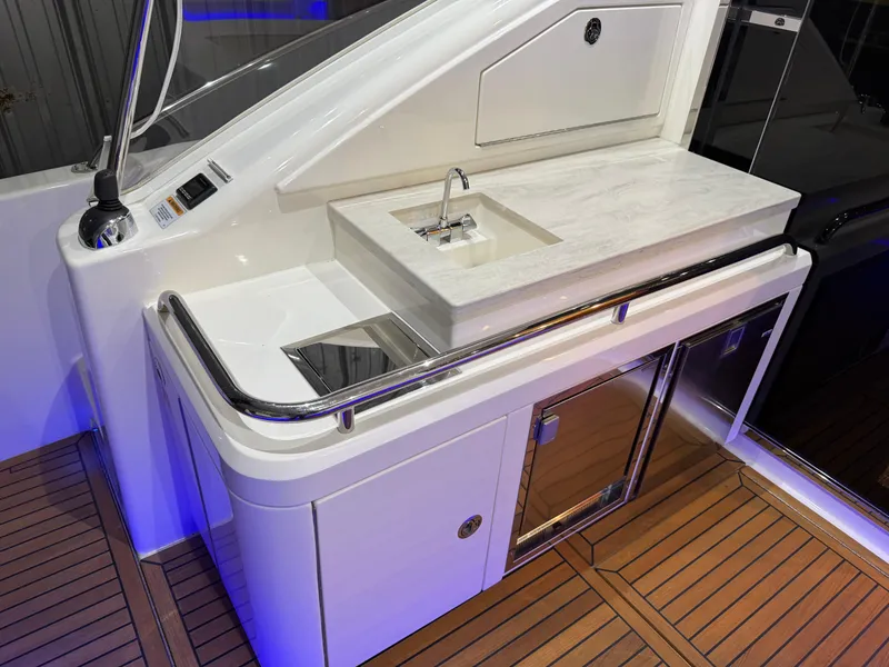 Slide: The Image of 2019 Riviera 4800 Sport Yacht kitchenette with sink, stove, and storage on teak flooring. - 27