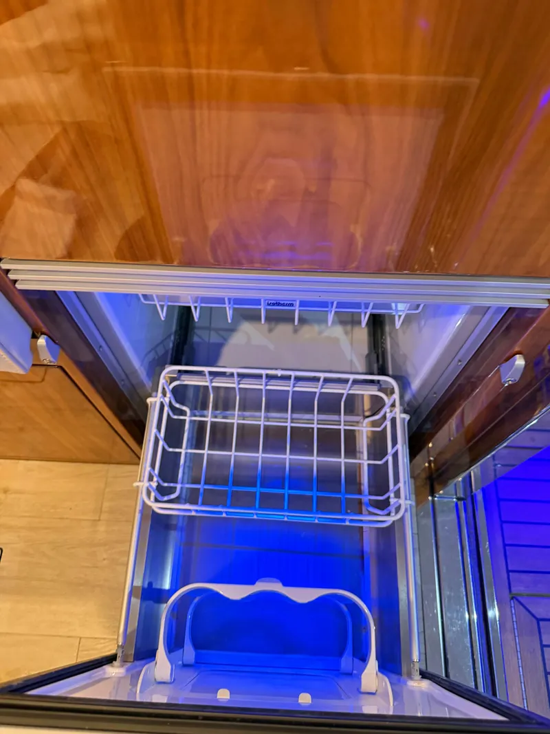 Slide: The Image of Open refrigerator drawer in 2019 Riviera 4800 Sport Yacht, featuring wooden paneling and blue lighting. - 47