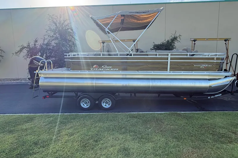 Slide: The Image of 2025 Sun Tracker Sportfish 24 XP3 pontoon boat on trailer, parked outdoors. - 2