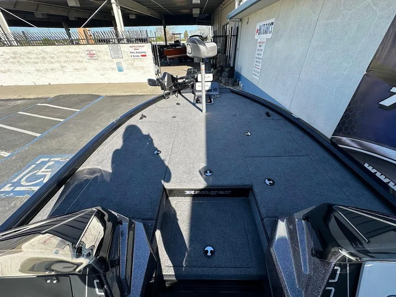Slide: The Image of 2025 Ranger ALPHA 208 boat deck with fishing equipment in a parking area. - 22