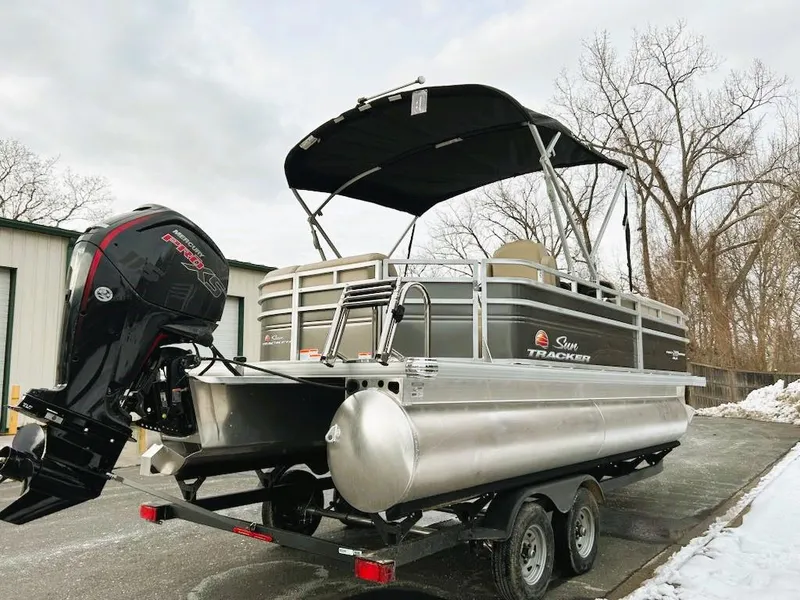 Slide: The Image of 2025 Sun Tracker Party Barge 20 DLX pontoon boat on trailer, parked outdoors. - 2