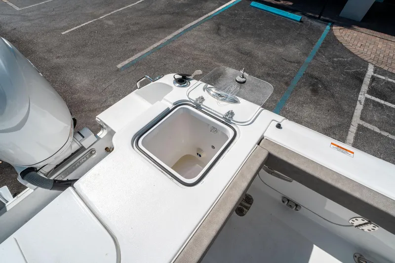 Slide: The Image of 2025 Sea Hunt Gamefish 25 boat deck with livewell and motor, parked on asphalt. - 14