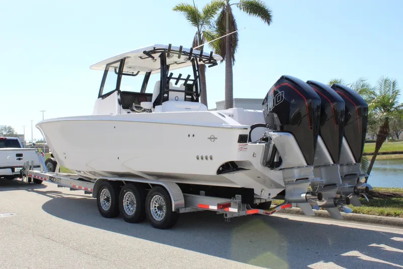 Slide: The Image of 2024 Fountain 32 NX boat on trailer with triple engines, parked near palm trees. - 13