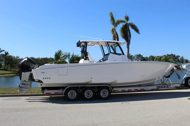Slide: The Image of 2024 Fountain 32 NX boat on trailer, parked near palm trees and water. - 17