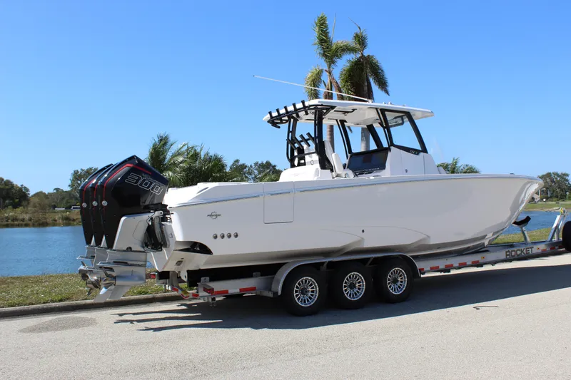 Slide: The Image of 2024 Fountain 32 NX boat on trailer by a lake, featuring triple outboard engines. - 18