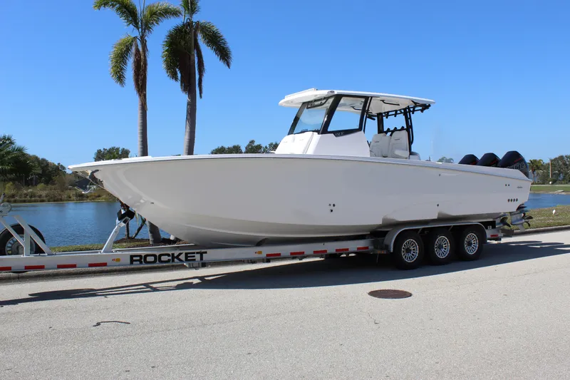 Slide: The Image of 2024 Fountain 32 NX boat on trailer, parked near palm trees and water. - 7