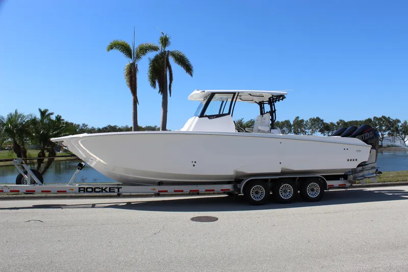 Slide: The Image of 2024 Fountain 32 NX boat on trailer, parked near palm trees and water. - 9