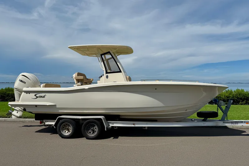 The Image of 2025 Scout 240 XSF boat on trailer, parked by waterfront under blue sky. - 0