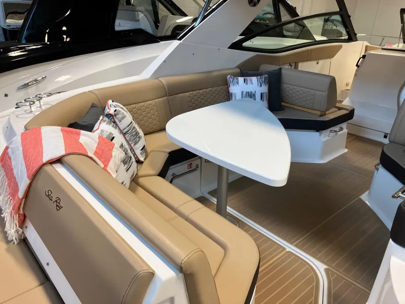 Slide: The Image of 2025 Sea Ray Sundancer 320 interior with beige seating, white table, and decorative pillows. - 7