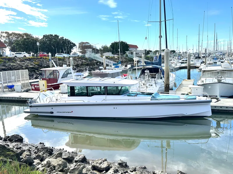 Slide: The Image of 2023 Axopar 37 XC Crosscabin boat docked in a marina under a clear blue sky. - 0