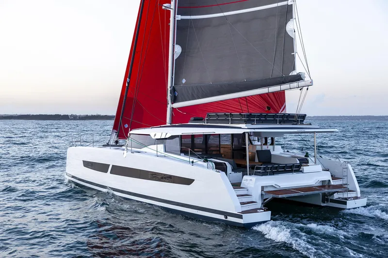 Slide: The Image of 2024 Fountaine Pajot Aura 51 catamaran sailing with red sails on open water. - 2